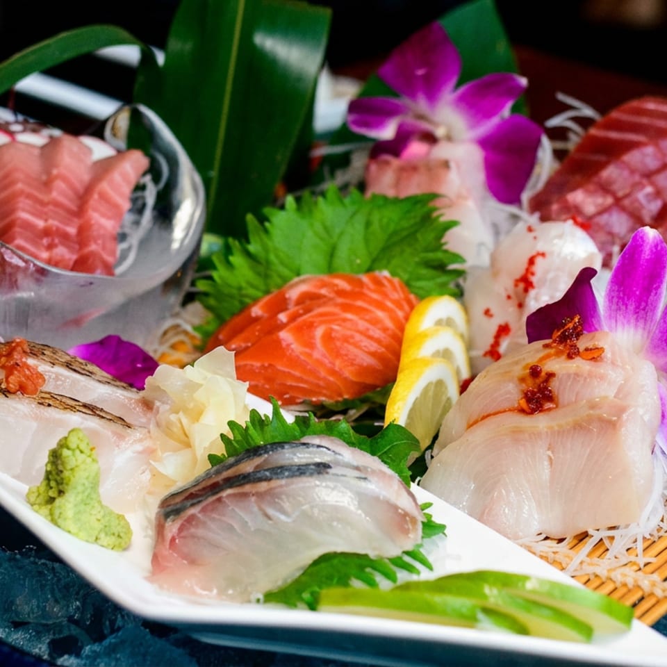 Assorted sashimi platter with salmon, tuna, white fish, shrimp, wasabi, lemon, shredded daikon, and orchids on crushed ice.