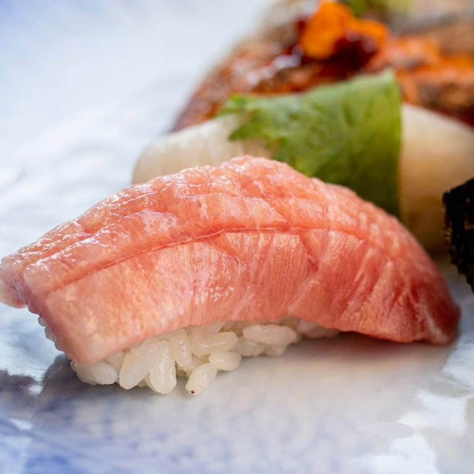 Close-up of assorted sushi, featuring pink tuna nigiri, shrimp sushi, and green garnish on a blue-and-white plate.